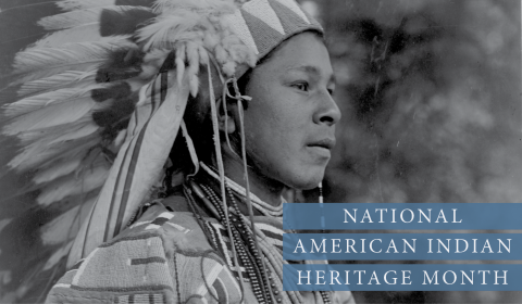 Black and white photographic portrait of an indigenous man in traditional feather head dress.