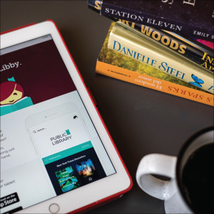 A tablet with the Libby app open, a stack of books and a coffee mug